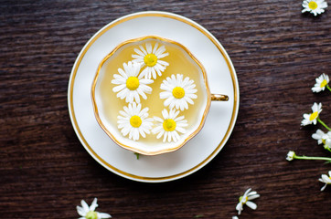 herbal camomile tea in a porcelain cup on a dark wooden background