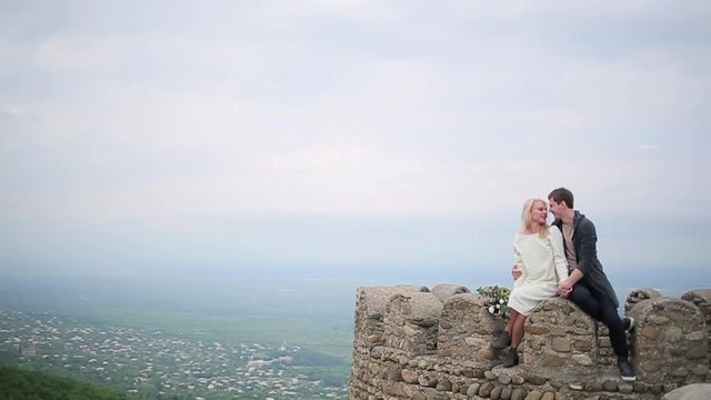 Couple sitting on the edge on the background of valley.