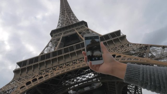 Low angle shot of a girl with smart phone making shot of Eiffel Tower, the main Paris landmark