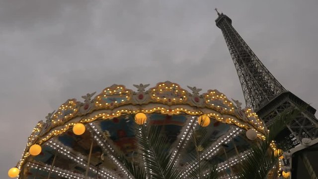Low angle shot of illuminated vintage merry-go-round and Eiffel Tower in the evening. Paris, France