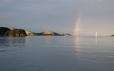 Naklejka na ściany i meble Rain clouds, sunshine and a rainbow: stormy weather for sailboats on the sea in the Bay of Islands, New Zealand, NZ.