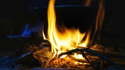 Burning fire with hot pot. Hot food preparation above burning wood pieces.