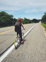 Fototapeta premium Red head woman riding bike along highway