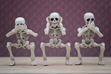 Three skeletons pose as three wise monkeys