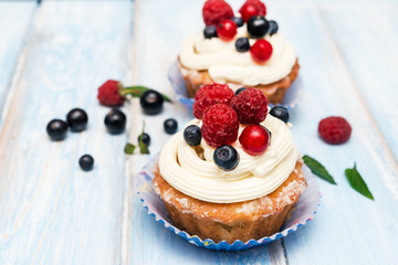 cupcakes decorated with cream cheese frosting and fresh berries on a wooden background