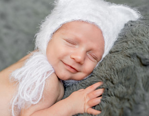 smiling sweet baby in white hat peacefully sleeping on gray blanket