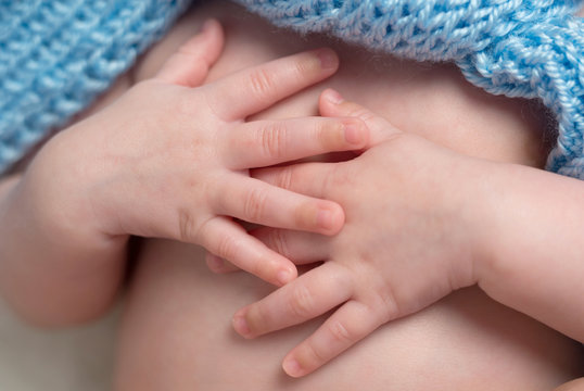 closeup of tender hands with tiny fingers of newborn baby coverd ith blue blanket