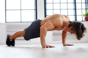 Athletic male doing pushups on a floor.