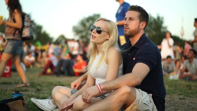 4k footage, young couple sitting in meadow enjoying summer music festival, crowd blurred
