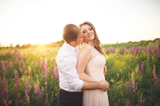 Bride holds groom's neck while he kisses her in the rays of sunset