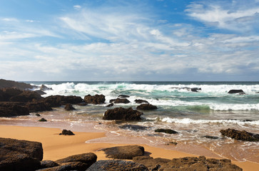 Fototapeta na wymiar The coast of the Atlantic Ocean. Volcanic stones on yellow sand. Beautiful seascape. Portugal, Algarve