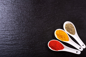 Naklejka premium various spices in ceramic spoons on dark background