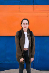 Young female traveler with backpack against of bright wall