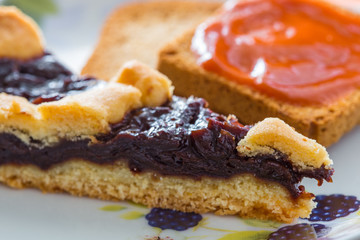 Fetta di crostata con marmellata di frutta e fette biscottate con marmellata di albicocche
