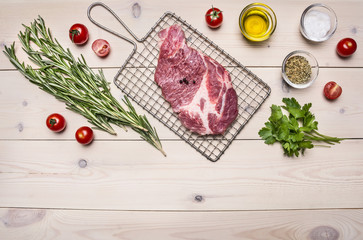 raw pork steak on the grill for cooking with rosemary, cherry tomatoes and spices, whole pepper border ,place for text  on wooden rustic background top view close up