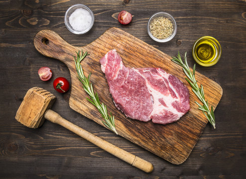 raw pork steak on vintage cutting board with rosemary, a wooden hammer for meat and spices