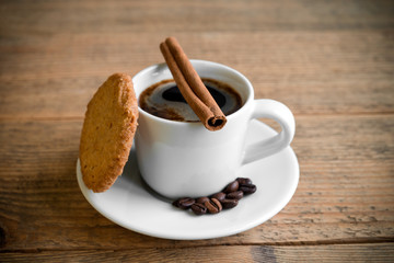 Black coffee in white cup with biscuit and cinnamon stick