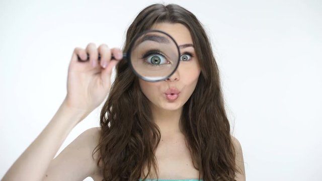 Beautiful young woman looking through a magnifying glass and making funny faces
