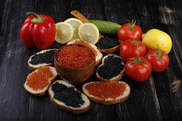red and black caviar with bread and vegetables on wooden background 