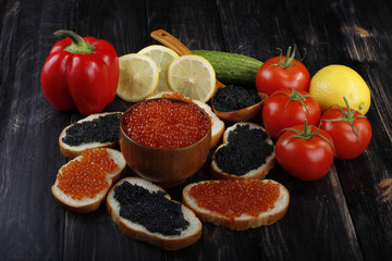 red and black caviar with bread and vegetables on wooden background 