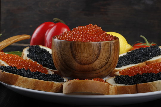 red and black caviar with bread and vegetables on wooden background 
