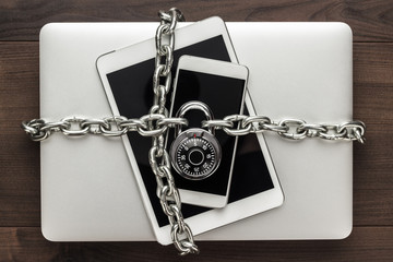 data security concept: computer, tablet, phone bound by metal chain and closed with combination lock on wooden table