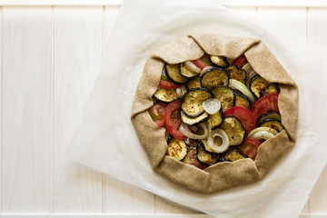 Homemade galette pie with grilled eggplants, tomatoes and onion on wooden background. Top view