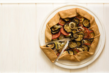 Homemade galette pie with grilled eggplants, tomatoes and onion on wooden background. Top view