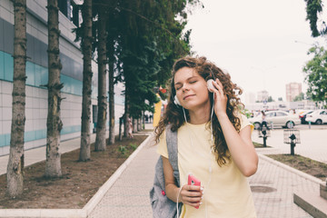 Fototapeta premium Curly brunette in a yellow T-shirt and headphones listening to m