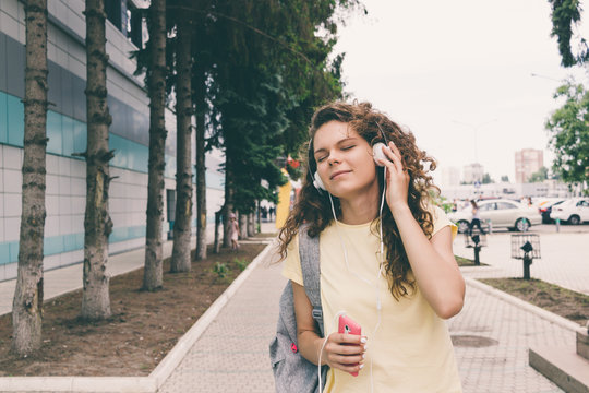 Curly brunette in a yellow T-shirt and headphones listening to m