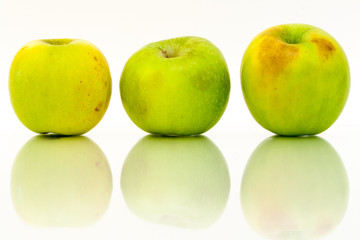 Three green apples in a row with reflections on a white background.