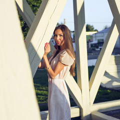 Portrait of a beautiful girl in  dress standing at the wooden pillars resting stare, fashion style, urban life, in  summer park on  bright sunny day. Business brunette woman outdoors.