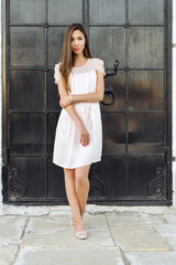 Beautiful woman standing at the black door of the castle, Gothic church . girl in a pink dress, posing close up, resting, fashion lifestyle, long hair, tanned skin.