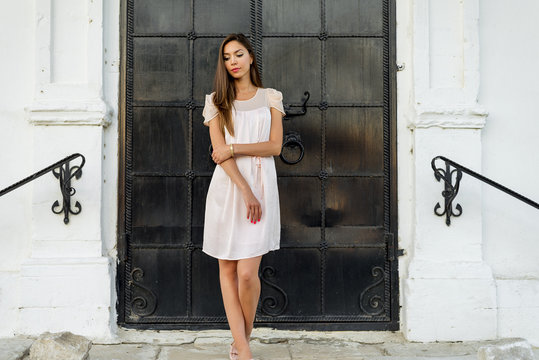 Beautiful woman standing at the black door of the castle, Gothic church . girl in a pink dress, posing close up, resting, fashion lifestyle, long hair, tanned skin. Outdoors enjoying.