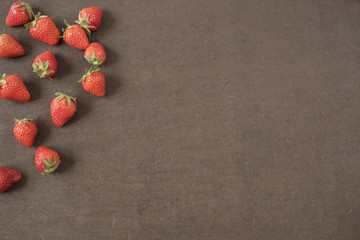 Border of whole fresh ripe red strawberries arranged on left sides on a dark textured slate background with copyspace. Fresh berry frame with copy space on right. 
