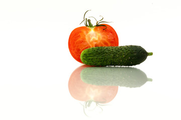Half of red tomatoes and fresh green cucumber with reflection on white background