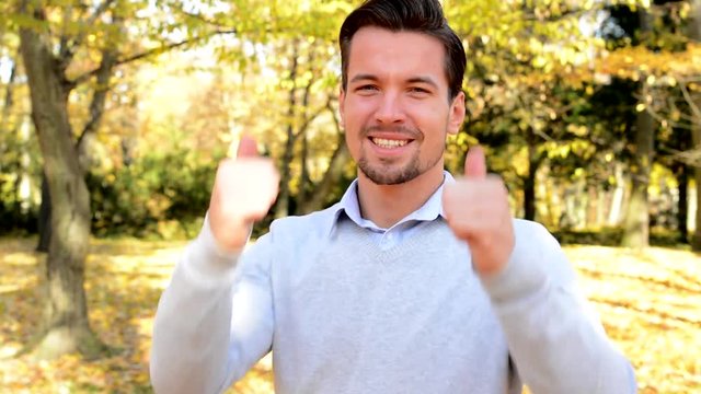 Young handsome man stands in the woods, smiles and shows two the thumbs-up
