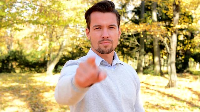 Young man stands in the woods and emphatically shows forefinger ahead.