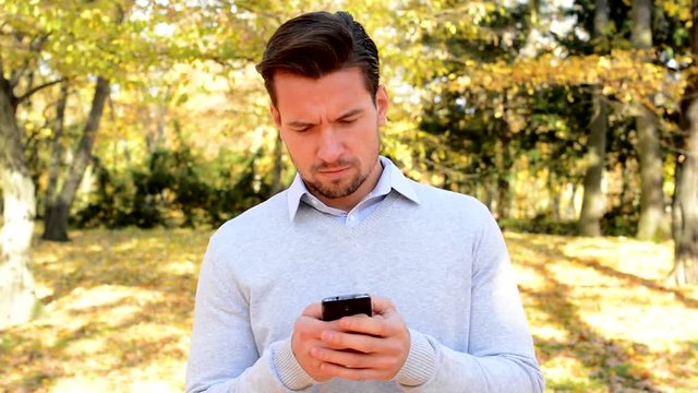 Young man stands in the woods, thinks about something and works  on the phone