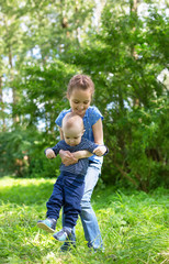 beautiful girl carrying a boy in a bright summer park, nice bokeh in background