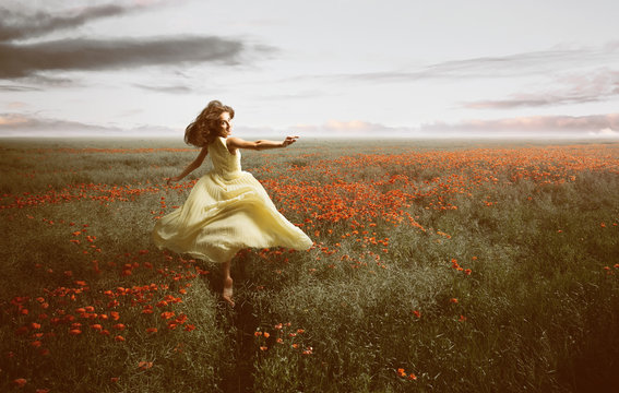 Frau im Kleid läuft freudig durch Mohnblumenfeld