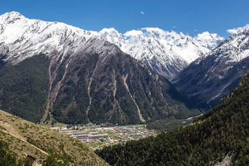 the mountain path and village in the valley on the background of snow-capped peaks