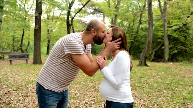 handsome man and pregnant woman kiss together in park 
