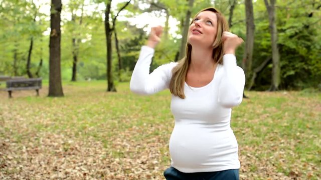 young happy pregnant woman rejoices in park 