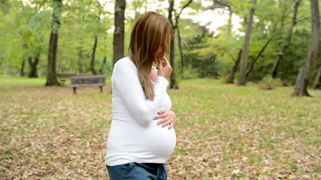 Young pretty pregnant woman walk around and think about something in park