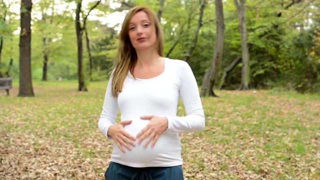Happy surprised young pregnant woman in park and smiles to camera
