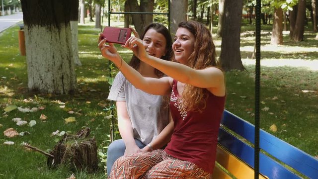 Happy girls taking selfie with the smartphone on a bench in the park