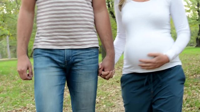 happy couple - pregnant woman with boyfriend walk in park - man strokes abdomen of woman - unknown person 