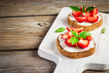 Fototapeta na wymiar Summer breakfast bruschetta with strawberries, basil and cottage