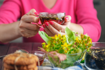 Woman with red nail polish holding tea cup with herbs